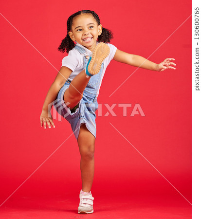 Happy, kick and excited girl in a studio with a casual, stylish and fashion kid outfit. Happiness, smile and young child with cool clothes kicking her leg with excitement isolated by a red background 130600766