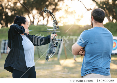 Archery, sports or help with a woman holding a bow and arrow outdoor for target practice with a coach. Coaching, learning or advice with a female and trainer at the shooting range for weapon training 130600966