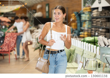 Girl buyer looks around in showroom of garden store and chooses suitable product Girl buyer looks around in showroom of garden store and chooses suitable product 130601138