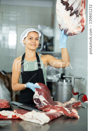 Positive young saleswoman demonstrating piece of meat in butcher shop Positive young saleswoman demonstrating piece of meat in butcher shop 130601232