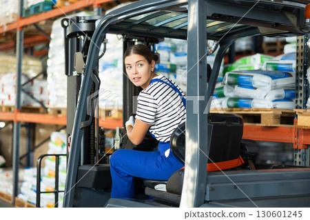 Girl works on fork lift loader in construction rack area warehouse store repair materials. 130601245
