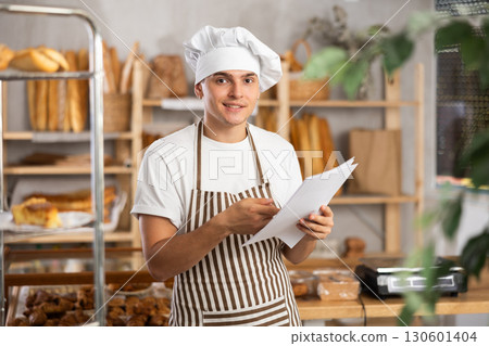 Cheerful young baker studying financial documents about profit in artisan bakery Cheerful young baker studying financial documents about profit in artisan bakery 130601404