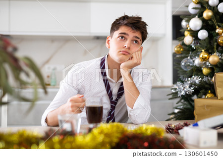 Young lonely man drinking alcohol at christmas table at home Young lonely man drinking alcohol at christmas table at home 130601450