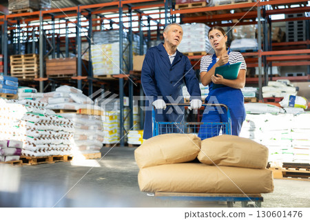 Girl checks papers invoices with mature man employee and revise availability of sacks goods in stock Girl checks papers invoices with mature man employee and revise availability of sacks goods in stock 130601476