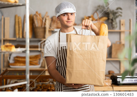 Young man entrepreneur owner of bakery holds out paper bag with pastries in hand 130601483
