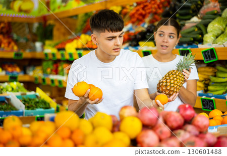 Male and female customers in casual clothes buying pineapples and oranges in grocery store 130601488