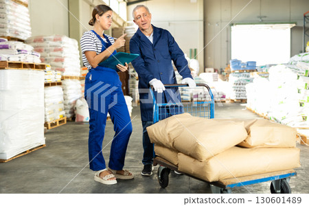 Girl checks papers invoices with mature man employee and revise availability of sacks goods in stock 130601489