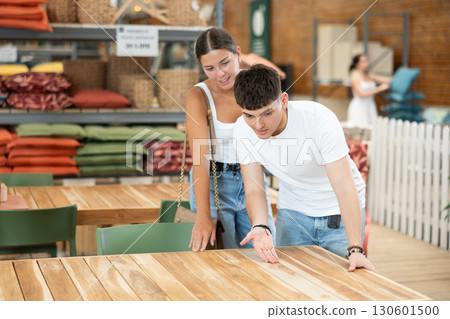 Interested young couple choosing wooden table in store 130601500