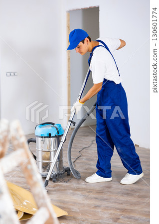 Young builder vacuuming floor while cleaning room in building after renovation Young builder vacuuming floor while cleaning room in building after renovation 130601774