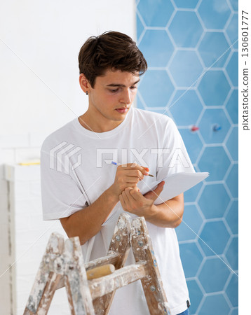 Young designer taking notes on papers while planning interior decoration Young designer taking notes on papers while planning interior decoration 130601777