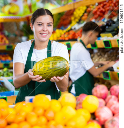 Positive young saleswoman holding fresh melon during offering fresh fruits Positive young saleswoman holding fresh melon during offering fresh fruits 130601843