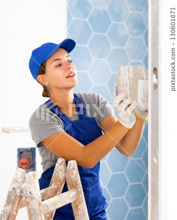 Professional female builder sticking ceramic tiles on wall in the bathroom being renovated Professional female builder sticking ceramic tiles on wall in the bathroom being renovated 130601871