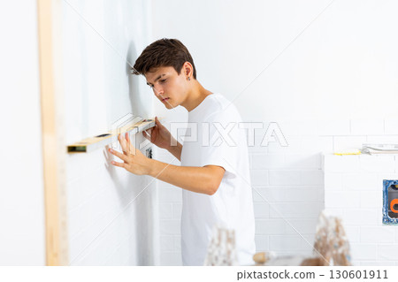 Guy inspecting quality of tiles laid on walls with level meter Guy inspecting quality of tiles laid on walls with level meter 130601911