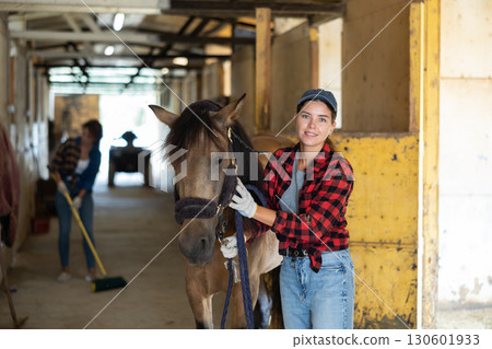 Female owner of horse takes animal out of stall, holds bridle and forces it to follow her Female owner of horse takes animal out of stall, holds bridle and forces it to follow her 130601933