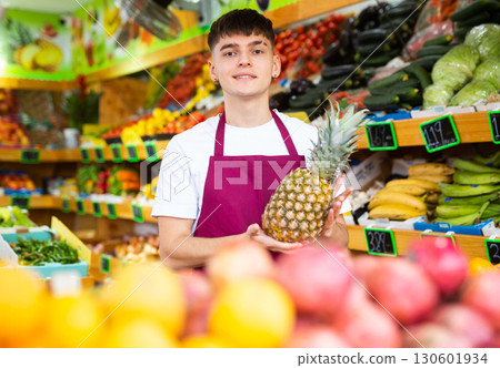Cheerful young seller man demonstrating pineapple in shop 130601934