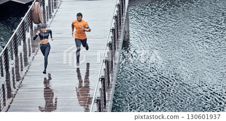 Overhead, fitness and man with woman running as exercise on city promenade training or workout outdoors in a town. Athlete, runner and fit male sprint fast for wellness, cardio and health by water 130601937