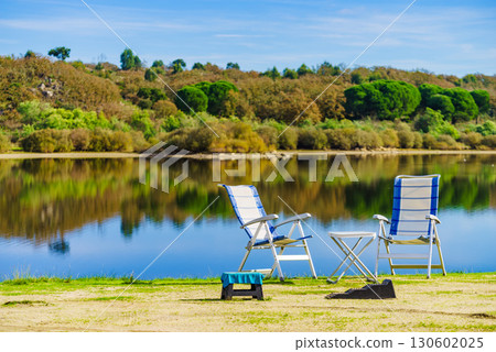 Two empty camp chairs on lake shore Two empty camp chairs on lake shore 130602025