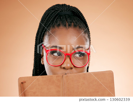 Black woman, notebook and hide face in studio for thinking, glasses or planning schedule for small business online. Young african entrepreneur, book or ideas for goal, vision or notes by background Black woman, notebook and hide face in studio for thinking, glasses or planning schedule for small business online. Young african entrepreneur, book or ideas for goal, vision or notes by background 130602339