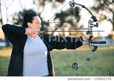 Hobby, learning and woman playing archery as a sport, outdoor activity and game in nature of France. Training, practice and girl with a bow and arrow for sports, competition and shooting at a park 130602376