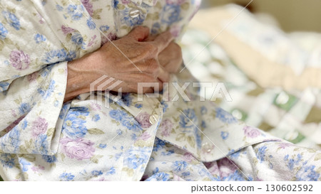 An elderly woman wearing pajamas and holding her stomach with both hands 130602592
