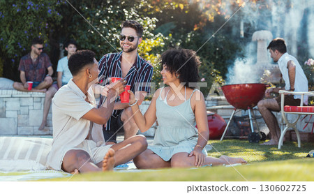 Party, diversity and toast with friends outdoor together at a bbq in summer for a social event or celebration. Alcohol, cheers or birthday with a young man and woman friend group celebrating outside 130602725