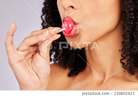 Black woman, lollipop and lipstick with face and beauty, hand with makeup and lip gloss on studio background. Lips, cosmetic product and candy in mouth, cosmetics advertising and cosmetology 130602822