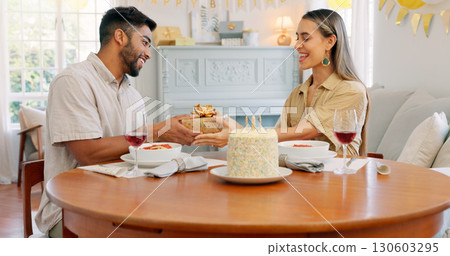 Birthday cake, giving gift and food with couple, love and date in home living room with drink. Happy, smile and people at table with conversation and celebration dessert with alcohol and talking 130603295