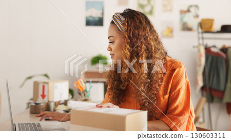 Woman, reading and laptop with boxes, logistics and e commerce for stock, boutique and order at startup. Designer, computer and typing for supply chain, shop and cardboard package for delivery on web 130603311