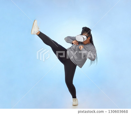 Black woman, kick and VR playing game, action or movement against blue studio background. African American female fighting, gaming or kicking in metaverse, 3D or virtual reality simulation on mockup 130603668