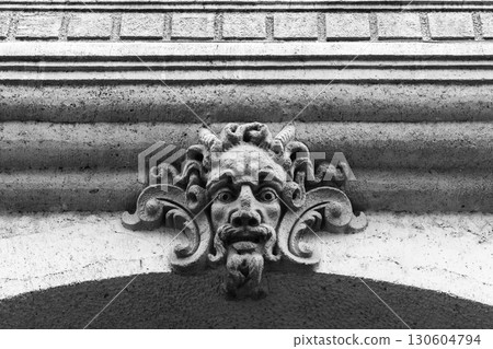 Architectural stone carving of a decorative face adorned with detailed features 130604794