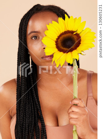 Portrait, beauty and sunflower with a black woman in studio on a beige background for natural treatment or body positivity. Spring, flower and skincare with a young female posing for wellness Portrait, beauty and sunflower with a black woman in studio on a beige background for natural treatment or body positivity. Spring, flower and skincare with a young female posing for wellness 130605231