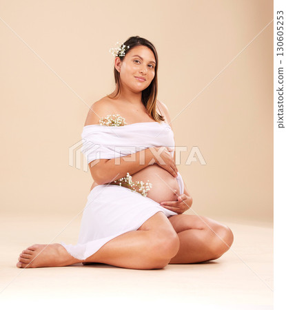 Pregnancy, beauty and portrait of a woman in studio with chiffon material and flowers holding her stomach. Maternity, prenatal health and pregnant female model with floral posing by beige background. 130605253