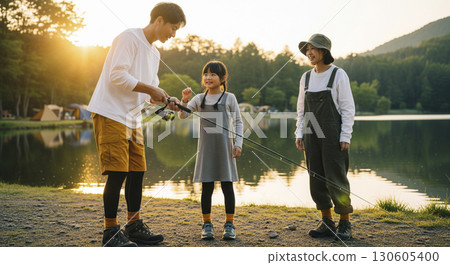 Father and son enjoying fishing by the lake, mother watching over them. Camping scene. 130605400