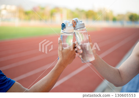 Two asian athlete men are holding and clinking their water bottles together on the racetrack. Two asian athlete men are holding and clinking their water bottles together on the racetrack. 130605553