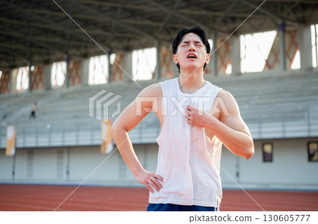 Asian man is standing with one hand on waist and other hand grabbing a white tank top. Hot or tired. 130605777