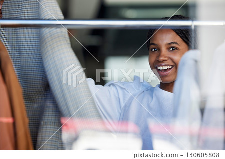 Shopping, clothes and face of black woman in store with choice on rack for sale, discount and promotion. Fashion, designer boutique and happy girl customer with clothing, outfit and retail products 130605808