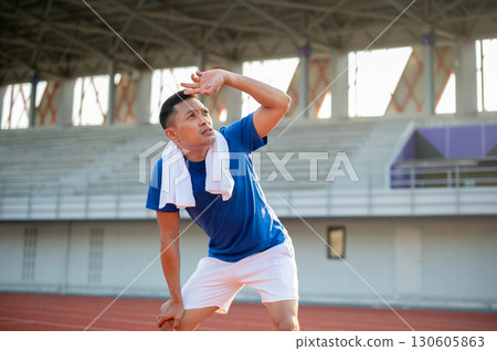 Asian man in blue t shirt is standing with hands on his knee and looking up with hand over eyes. Asian man in blue t shirt is standing with hands on his knee and looking up with hand over eyes. 130605863