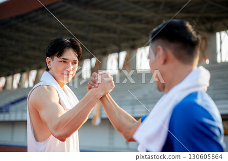 Two asian men are joining hands and locking eyes with each other on racetrack. Good sportsmanship. Two asian men are joining hands and locking eyes with each other on racetrack. Good sportsmanship. 130605864