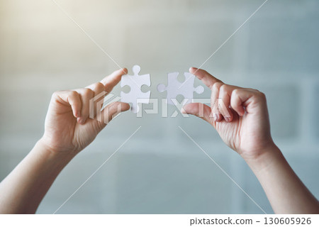 Hands, puzzle and synergy with a business woman in the office against a brick wall for building or connection. Idea, innovation and strategy with a female employee holding jigsaw pieces at work 130605926