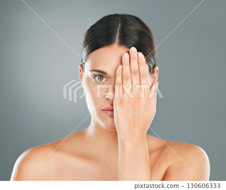 Face, cover and portrait of a woman with a hand on eye isolated on a grey studio background. Skincare, beauty and serious model hiding eyes for dermatology, skin problem and cosmetics on a backdrop 130606333