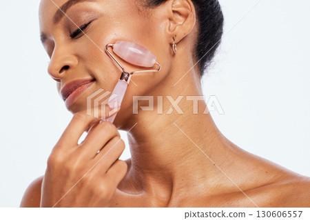 Beauty, jade roller and massage for a woman in studio for dermatology, skincare and natural skin. Aesthetic model person with facial stone tools for healthy glow isolated on a white background Beauty, jade roller and massage for a woman in studio for dermatology, skincare and natural skin. Aesthetic model person with facial stone tools for healthy glow isolated on a white background 130606557