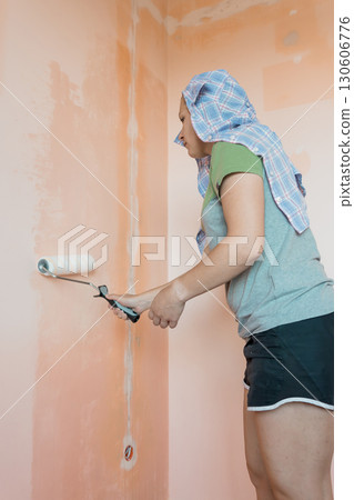 Woman Painting Peach-Colored Wall Interior with Roller. Home Renovation DIY Project, Light Colors, Textured Surface, Indoor Scene, Casual Attire 130606776