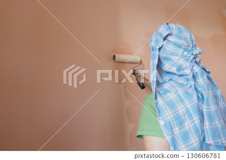 Interior Home Painting Project: Person in Blue Shirt Rolling Beige Wall, DIY Renovation, Light Brown Decor, Plaid Cloth Protection Interior Home Painting Project: Person in Blue Shirt Rolling Beige Wall, DIY Renovation, Light Brown Decor, Plaid Cloth Protection 130606781