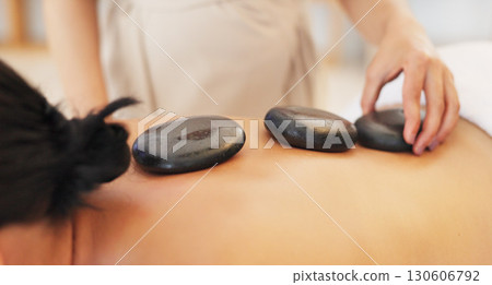 Woman, spa bed and back with hot stone massage, care or professional treatment for muscle, stress or wellness. Girl, masseuse or rock for physical therapy, spine and closeup at luxury resort for body Woman, spa bed and back with hot stone massage, care or professional treatment for muscle, stress or wellness. Girl, masseuse or rock for physical therapy, spine and closeup at luxury resort for body 130606792