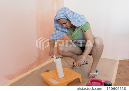 Woman Painting Interior Wall Peach Color. DIY Home Renovation. Roller. Bucket. Protective Cloth. Interior Design. Light Wood Floor. 130606838
