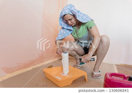 Woman Painting Peach-Colored Wall Indoors, DIY Home Renovation, Roller, Protective Cloth, Casual Attire, Light-Colored Room, Bright Daylight 130606841