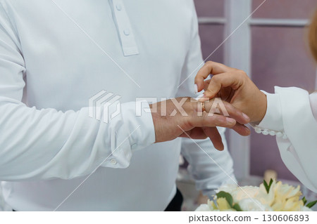 Wedding Ceremony Ring Exchange, Groom Placing Band on Bride's Finger, White Attire, Intimate Moment, Love, Floral Background, Soft Lighting Wedding Ceremony Ring Exchange, Groom Placing Band on Bride's Finger, White Attire, Intimate Moment, Love, Floral Background, Soft Lighting 130606893