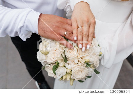 Wedding Rings on Hands with Bouquet, Marriage Symbolism, White Roses, Elegant Ceremony, Love, Commitment, Romance, Neutral Tones, Close-Up Shot Wedding Rings on Hands with Bouquet, Marriage Symbolism, White Roses, Elegant Ceremony, Love, Commitment, Romance, Neutral Tones, Close-Up Shot 130606894