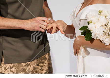 Military Wedding Ceremony. Emotional Ring Exchange. Olive Green Uniform, White Dress, Bouquet, Hand Close-Up, Symbolic Love, Realistic Style. Military Wedding Ceremony. Emotional Ring Exchange. Olive Green Uniform, White Dress, Bouquet, Hand Close-Up, Symbolic Love, Realistic Style. 130606895