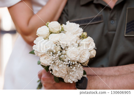 Bridal Bouquet Held by Military Man in Uniform, Wedding Ceremony, White Roses, Romantic Gesture, Patriotic Love, Close-Up Shot. 130606905